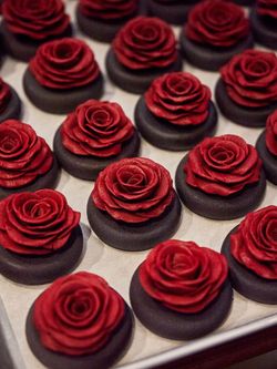 Dark chocolate bases topped with intricately crafted red rose-shaped decorations, arranged in neat rows.