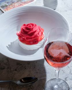 A dessert featuring a rose-shaped strawberry topping on a meringue base, accompanied by a glass of sparkling rose.