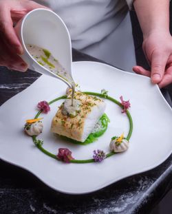 Poached fish served with rice and seaweed, garnished with flowers and sauce being poured on top at Le Pavillon.