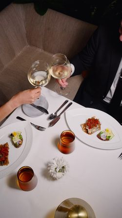 Two people toasting with white wine glasses at a fine dining table with gourmet dishes and white tablecloth at Le Pavillon.