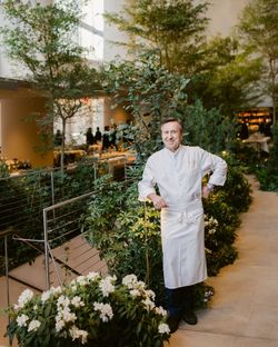 A chef stands amidst greenery inside Le Pavillon, showcasing the restaurant's elegant ambiance and fine dining experience.