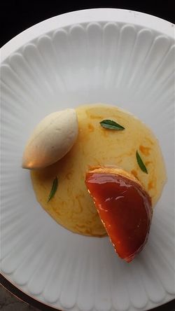 Caramel-glazed tart slice with vanilla cream and sauce garnished with green leaves on a white plate at Le Pavillon.