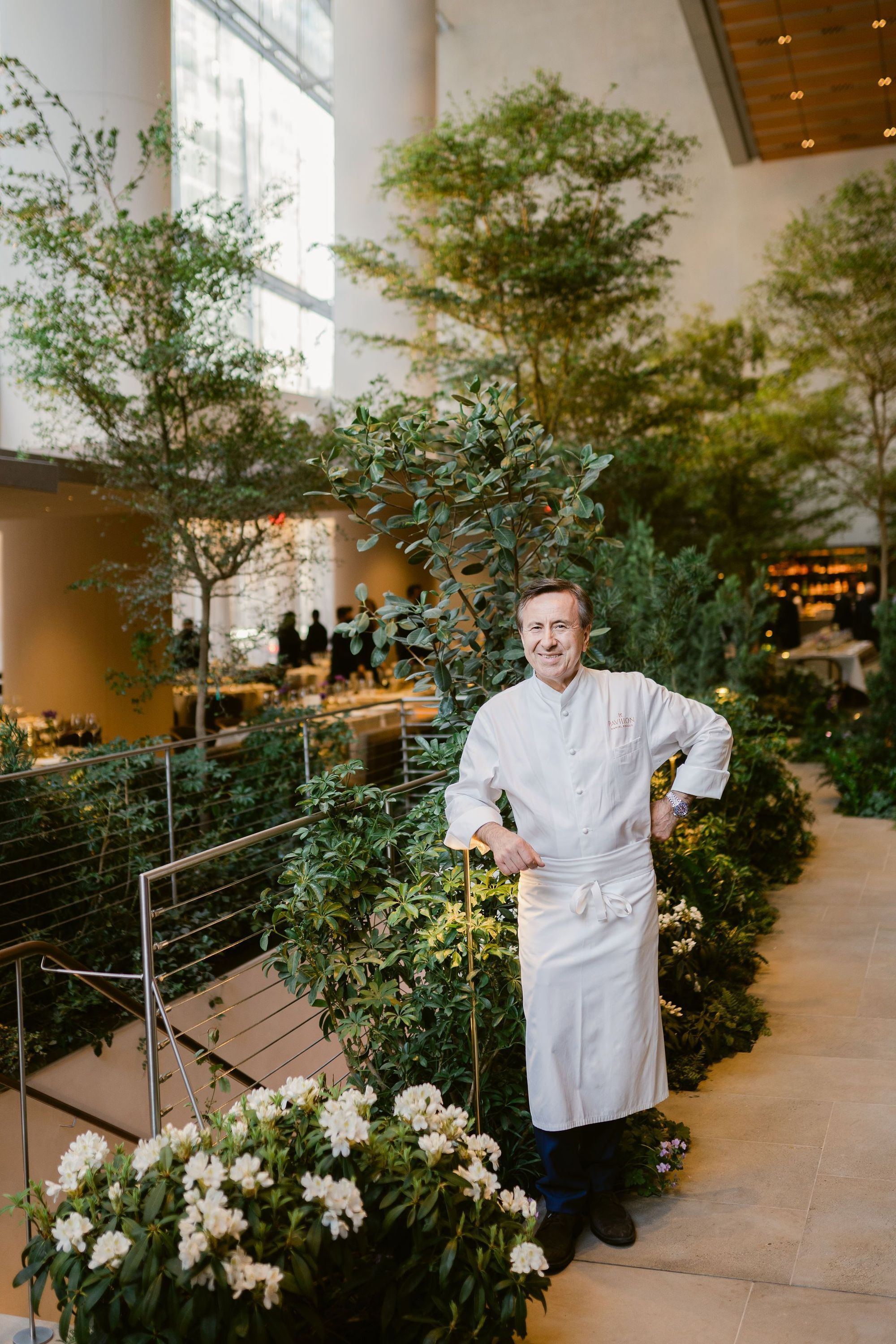 A chef in a white uniform stands among lush greenery in a spacious dining area, showcasing contemporary design.