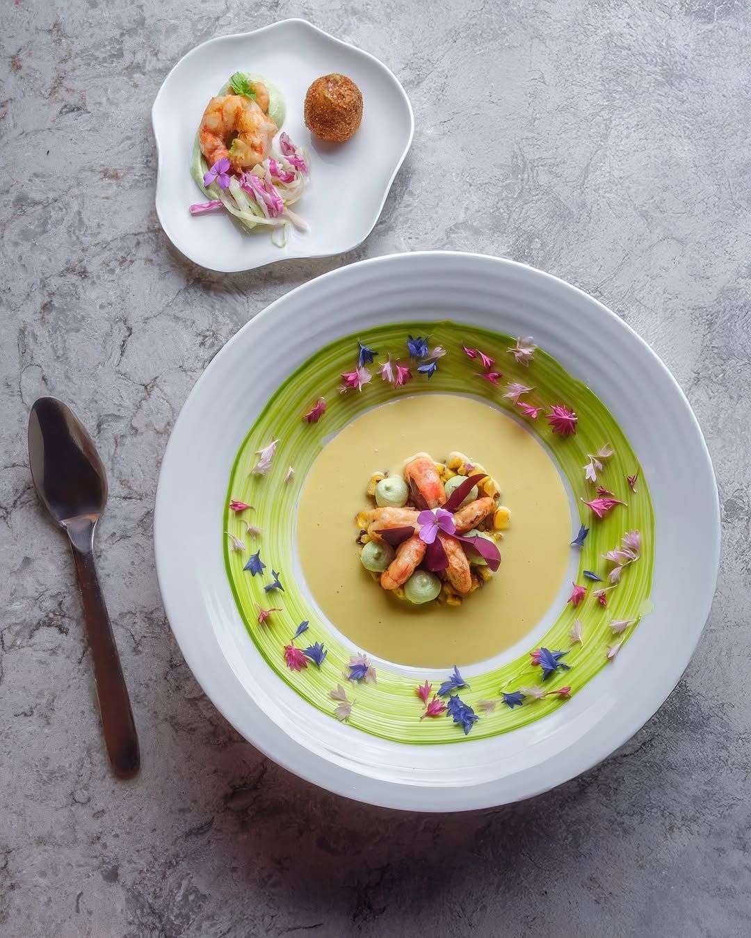 A beautifully plated dish featuring colorful garnishes, floral accents, and a side of delicately prepared seafood.